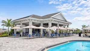 Ein Poolbereich mit überdachter Sitzgelegenheit, Sonnenschirmen und Liegestühlen.
