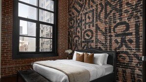 Un dormitorio con pared de ladrillo, un ventanal grande, una cama con cabecera y un banco.