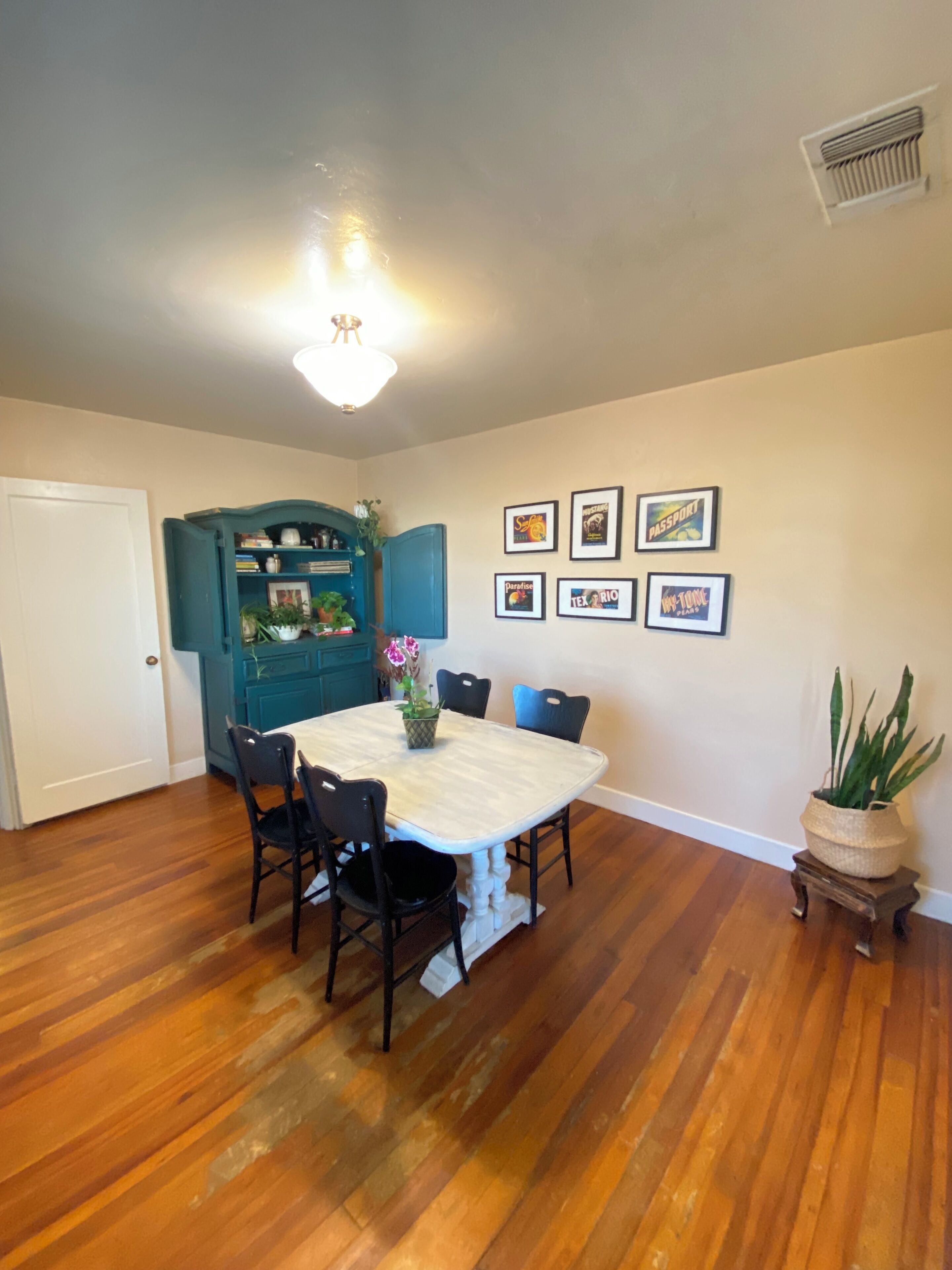 A dining room with a white table, black chairs, teal cabinetry, and framed pictures on the wall.