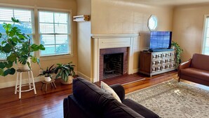 Un salon avec une cheminée, un téléviseur posé sur un meuble en bois et plusieurs plantes en pot.