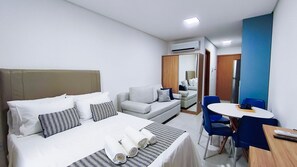 Una camera d'albergo con un letto, un divano, un tavolo da pranzo con sedie, un condizionatore d'aria e uno specchio.