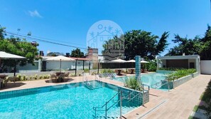 Une piscine avec une terrasse carrelée, des sièges d’extérieur et un ciel dégagé.
