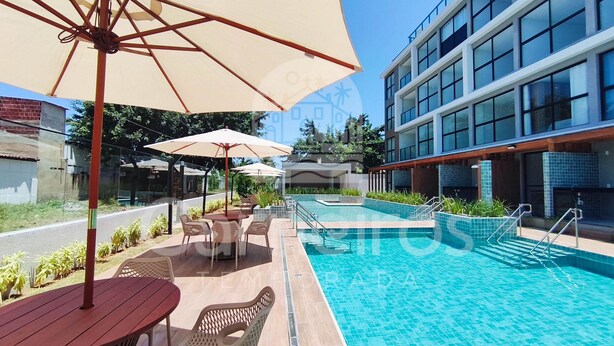 A swimming pool with a tiled deck, surrounded by outdoor seating and umbrellas. - Acqua Beach Residence (Tamandaré)