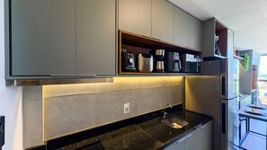 Una cocina moderna con armarios grises, cafetera integrada y pileta de acero inoxidable.
