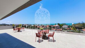 A rooftop terrace with outdoor seating, a view of the sea, and a building silhouette in the background. - Acqua Beach Residence (Tamandaré)