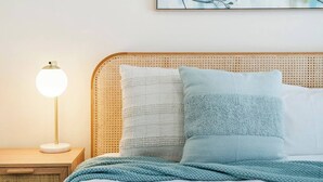 Ein ordentlich bezogenes Bett mit blauer Decke, einer Nachttischlampe und einem gewebten Kopfteil.