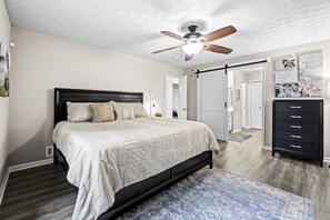 A bedroom with a bed, a ceiling fan, a dresser, and a door leading to another room. - Lake Lanier Escape - Gainesville Lakefront stay (Gainesville)