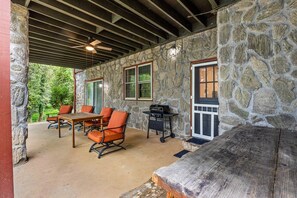 A covered outdoor patio with stone walls, a wooden table, orange chairs, and a barbecue grill. - Lake Lanier Escape - Gainesville Lakefront stay (Gainesville)