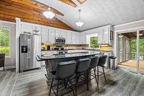 A modern kitchen with a central island, bar stools, stainless steel appliances, and a view to the outdoors.