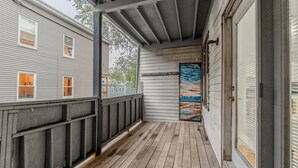 Eine überdachte Veranda mit Holzboden, Blick auf ein Haus mit weißer Fassade und einer Tür, die ein Landschaftsbild zeigt.