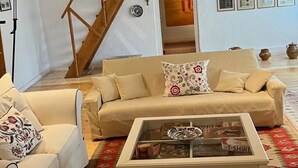 Un salón acogedor con techo de madera, un sofá color beige, una mesa de centro blanca y una escalera.