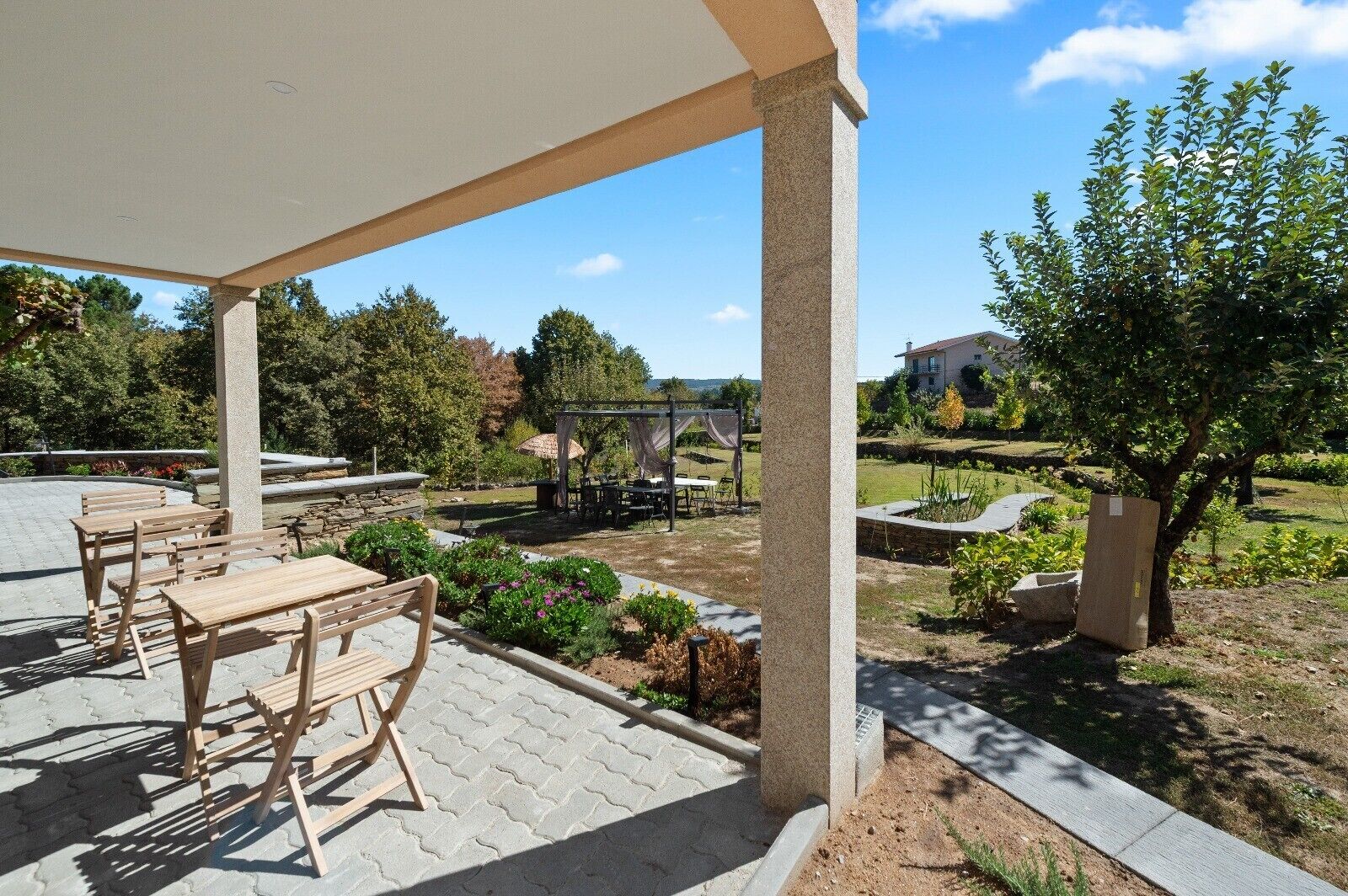 Eine überdachte Terrasse im Freien mit Holzmöbeln, einer Pergola und einem Gartenbereich.