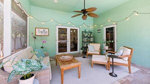 A cozy patio area with wicker furniture, a ceiling fan, string lights, and a 'together' sign. - Sunshine and Serenity Holidays (Boynton Beach)