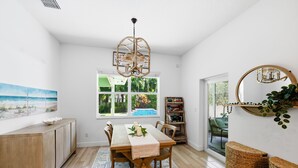 A dining area with a wooden table, chairs, a chandelier, a bookshelf, and a view of the outdoors. - Sunshine and Serenity Holidays (Boynton Beach)