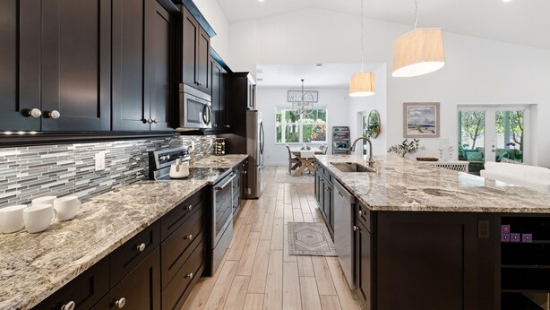 A modern kitchen with dark cabinetry, granite countertops, and a central island. - Sunshine and Serenity Holidays (Boynton Beach)