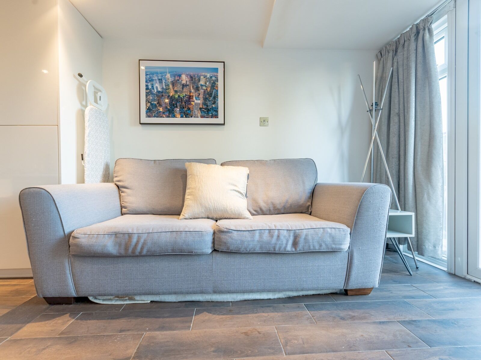 Een moderne woonkamer met een grijze bank, een gepresenteerd stadsbeeld en een raam van de vloer tot aan het plafond met gordijnen.