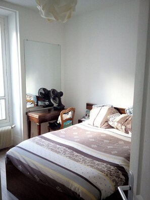 Ein Schlafzimmer mit Bett, Schreibtisch, Stuhl, Spiegel und Heizkörper.