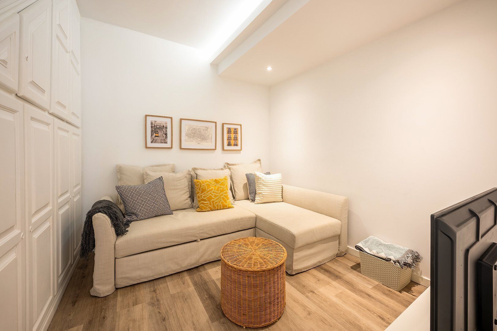 A cozy living room with a beige sofa, a wicker ottoman, and a small side table.