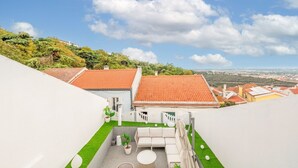 A rooftop terrace with a white railing, green artificial grass, and a seating area with a table and chairs.
