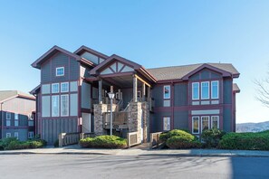 A two-story house with a stone facade, a covered front porch, and a clear view of the surrounding landscape. - Grand Oaks RQ6- Mountain Condo, Gated Resort, Indoor/Outdoor Pools & Hot Tub (Banner Elk)