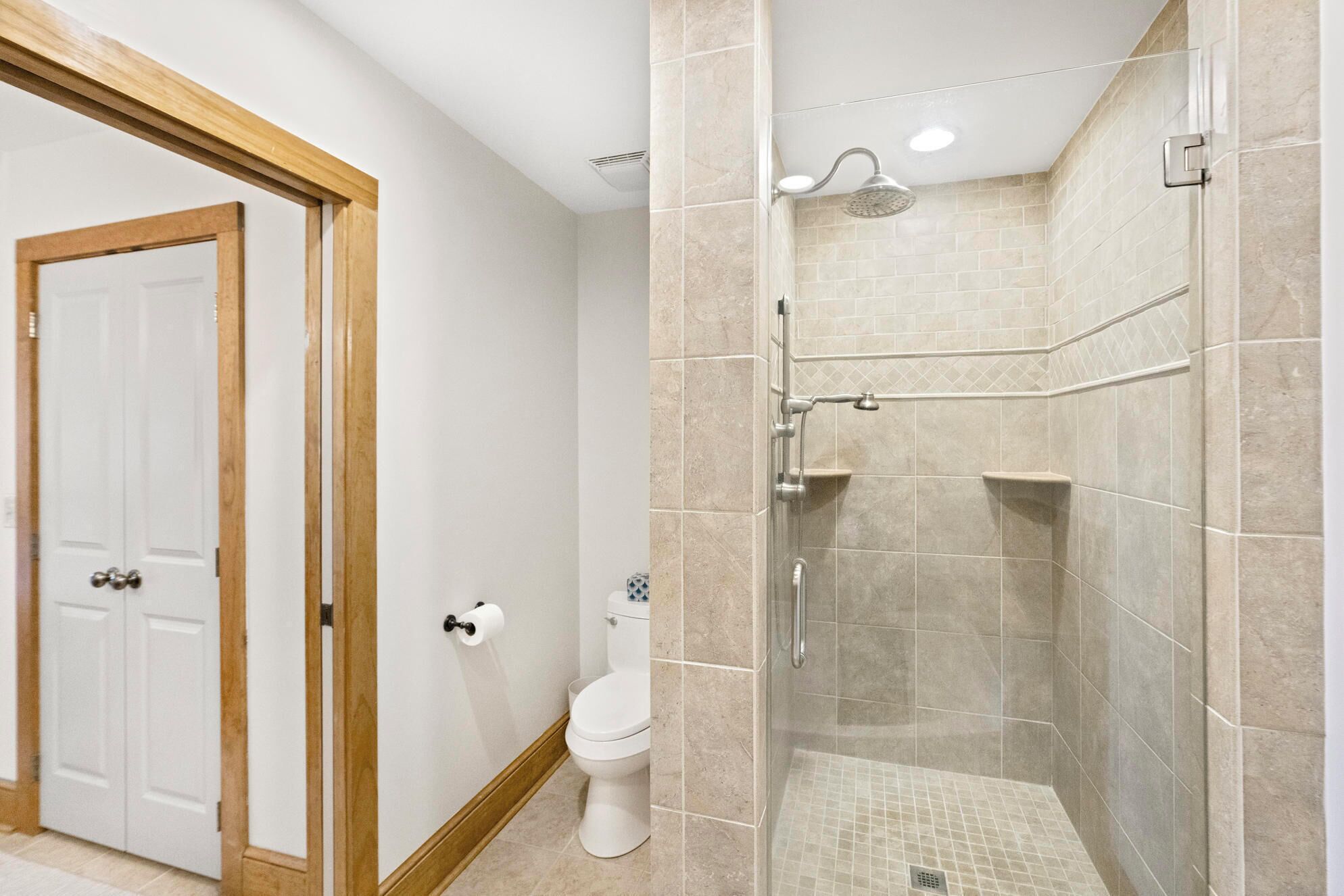 A bathroom with a toilet, a shower with a glass door, and beige tiled walls.