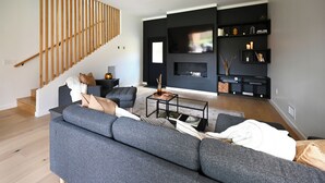 Uma sala de estar moderna com um sofá cinzento, uma mesa de centro e uma TV fixada numa parede preta.