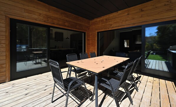 A wooden deck with a table and chairs, large sliding glass doors, and a view of a garden. - Modern Mountain View Chalet in Windham (Windham)