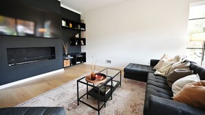Uma sala de estar moderna com um sofá preto, uma mesa de centro de vidro e uma lareira.