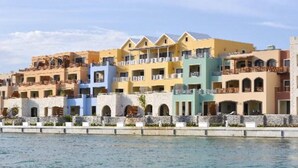 Una hilera de edificios hoteleros coloridos con balcones, un muro de piedra al frente y una masa de agua en primer plano.