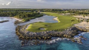Un campo de golf costero con una masa de agua, calles verdes, bunkers de arena y un litoral rocoso.