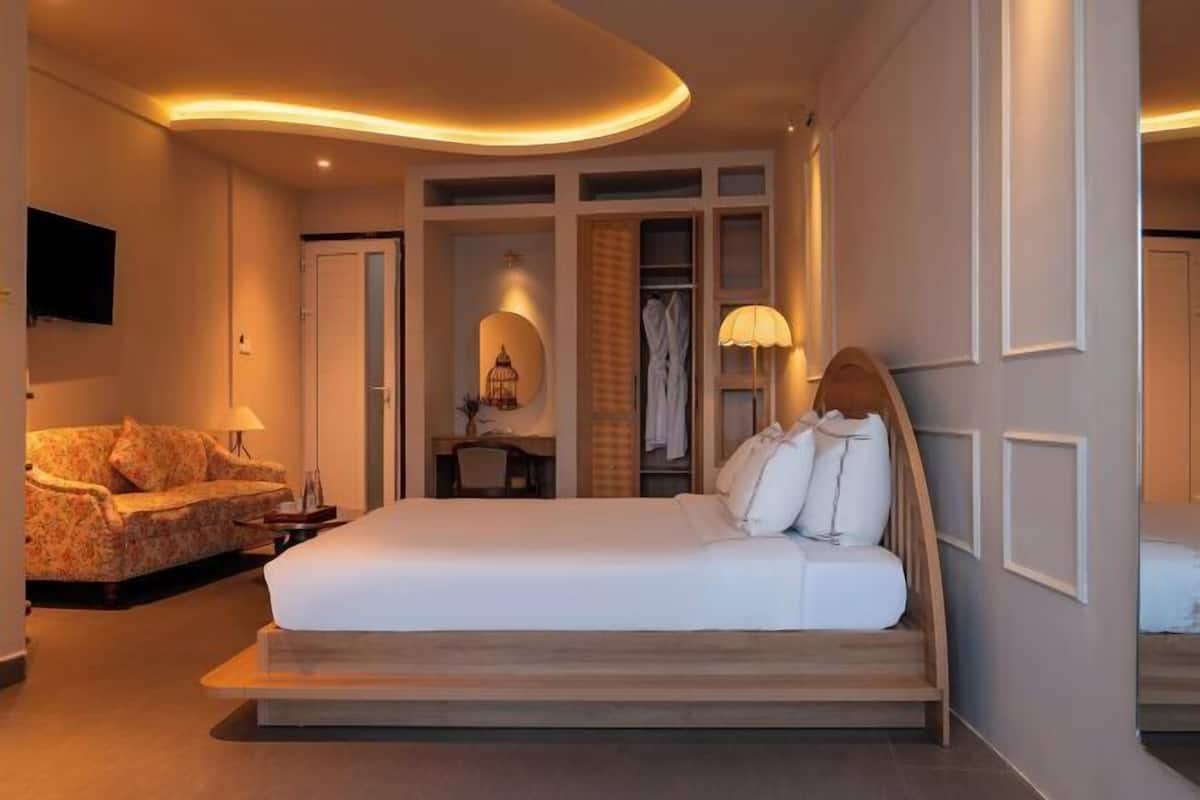A hotel room with a bed, a sofa, a desk, a wardrobe, and a television.