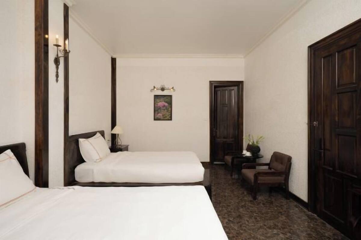 A hotel room with two single beds, a small table with a lamp, a chair, and a door.