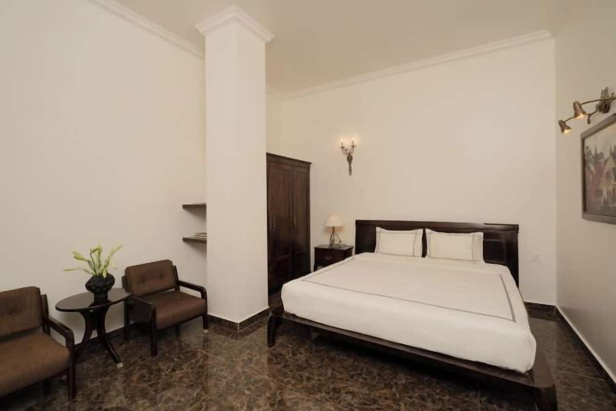 A hotel room with a large bed, two armchairs, a small table with a plant, a nightstand with a lamp, and a wall-mounted light fixture.