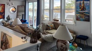 Een ruime woonkamer met een hoge plafond, grote ramen en een plafondventilator.