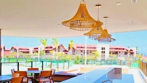 A poolside area with a stone bench, tables, chairs, and hanging wicker lamps. - Makia Beach Experience Resort - Muro Alto, Porto de Galinhas - B18 POOL FRONT (Ipojuca)