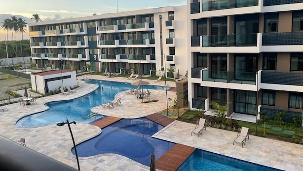 A modern hotel with a swimming pool, multiple balconies, and a landscaped outdoor area. - Makia Beach Experience Resort - Muro Alto, Porto de Galinhas - B18 POOL FRONT (Ipojuca)