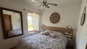 A bedroom with a bed, a ceiling fan, a mirror, a bedside table, and a window with curtains. - Le Panorama with views of the Valley (Soultzeren)