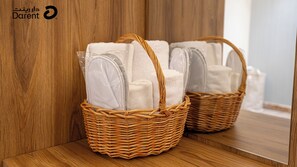Deux paniers en osier dotés de poignées, chacun contenant des serviettes blanches pliées, sont posés sur une surface en bois, adossés à un mur en bois.