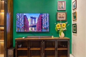 Ein Fernseher an einer grünen Wand, ein Holzschrank mit einem Lautsprecher und eine Vase mit Sonnenblumen.