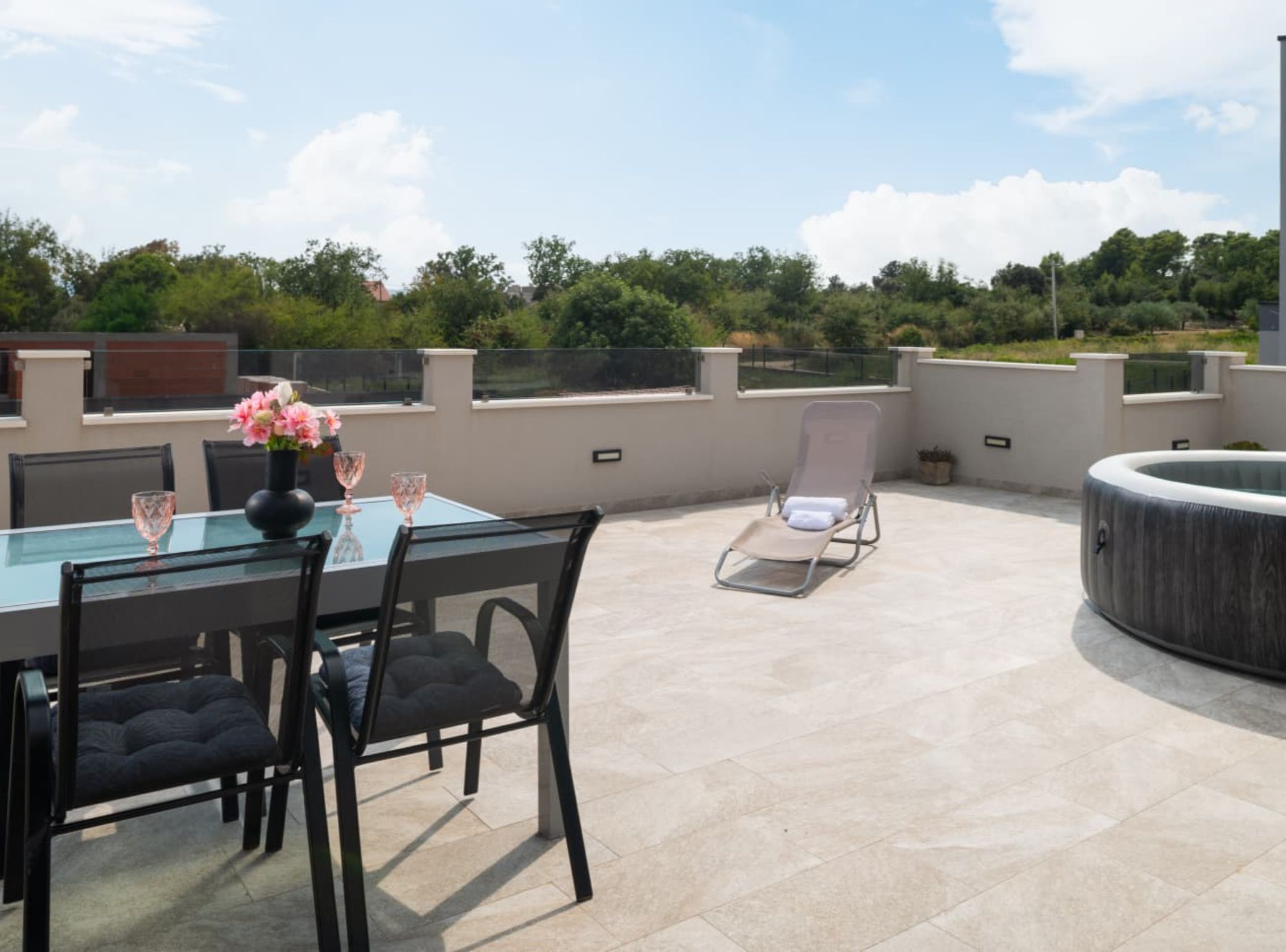 Een dakterras met een glazen tafel, stoelen en een loungestoel.