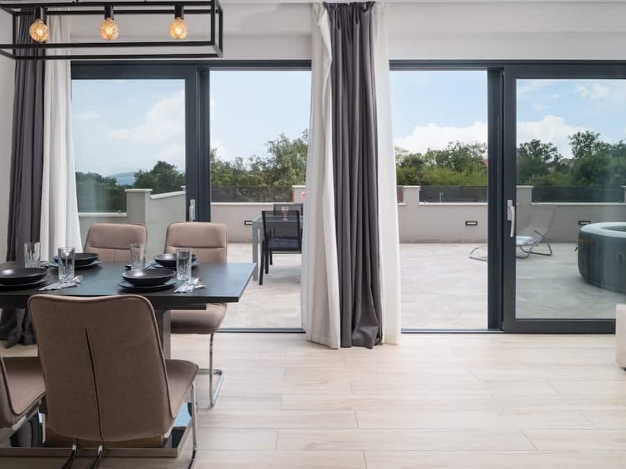 A modern dining area with a table set for four, large windows, and a view of the outdoors.