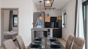 Un comedor moderno con una mesa oscura dispuesta para seis personas, una cocina al fondo y una pequeña decoración con forma de velero.