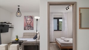 Una sala moderna con un sofá, una mesa de centro y un televisor. Hay un cuadro en la pared y un frutero sobre la mesa.