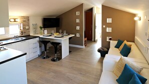 Une cuisine moderne avec un coin repas, un téléviseur à écran plat et un salon doté d’un canapé et de coussins.