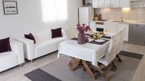 Un salon moderne et bien éclairé, avec un coin repas, des meubles blancs et une cuisine en arrière-plan.