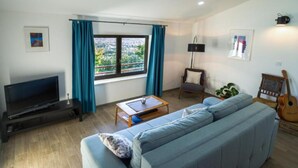 A living room with a sofa, a coffee table, a TV, a chair, a guitar, and a window with curtains. - Istra Green Soul Apartment (Oprtalj)