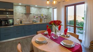 A modern kitchen with a dining area, featuring a brick backsplash, stainless steel appliances, and a large window with a balcony view. - Istra Green Soul Apartment (Oprtalj)