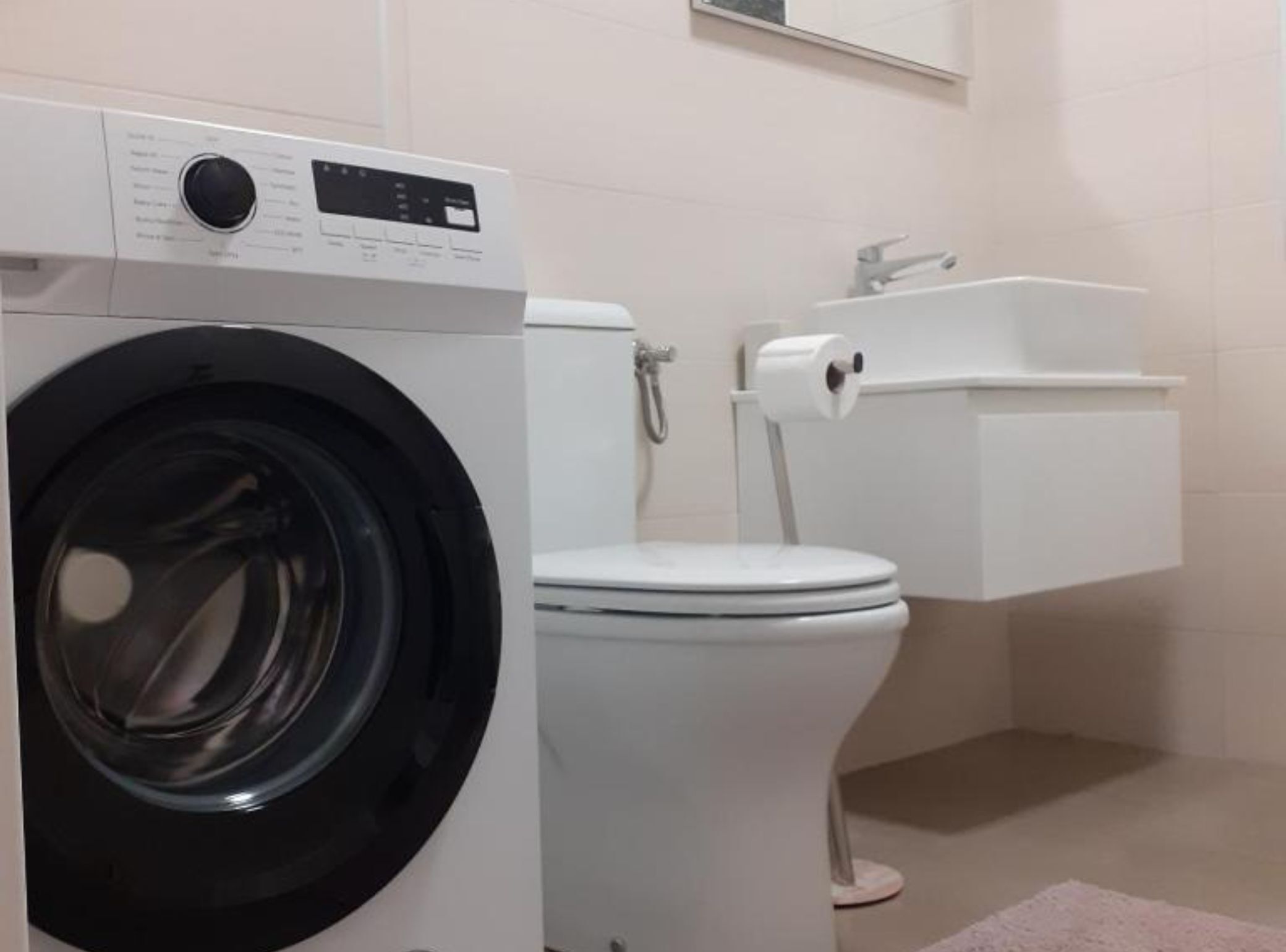 Une petite salle de bain équipée d’un lave-linge à chargement frontal, de toilettes et d’un lavabo.