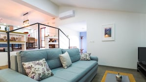 A living room with a sofa, a coffee table, and a TV. There is a staircase leading to an upper level with a dining area. - Istra Green Soul Apartment (Oprtalj)