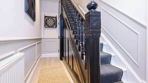 Una escalera con barandilla negra y un remate decorativo, que lleva a un rellano alfombrado.